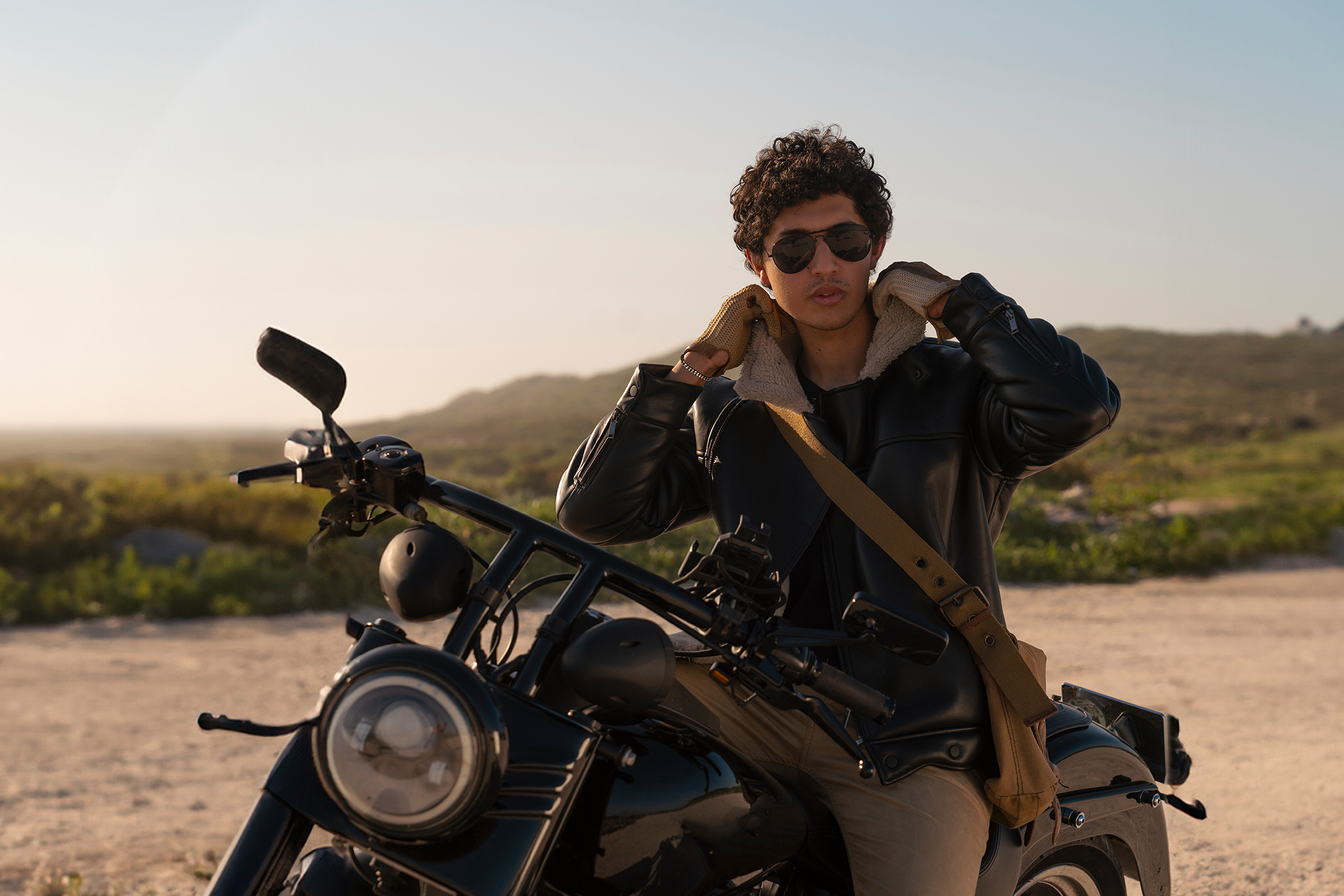 A man wearing sunglasses sits confidently on a motorcycle, showcasing a relaxed and stylish demeanor